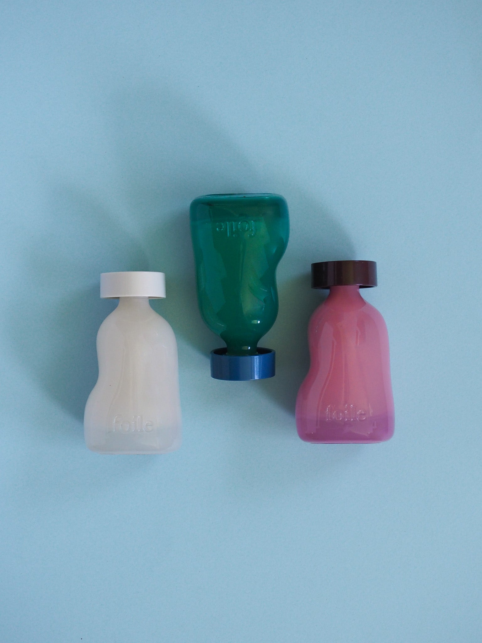 Three bottles of different colors on a light blue background